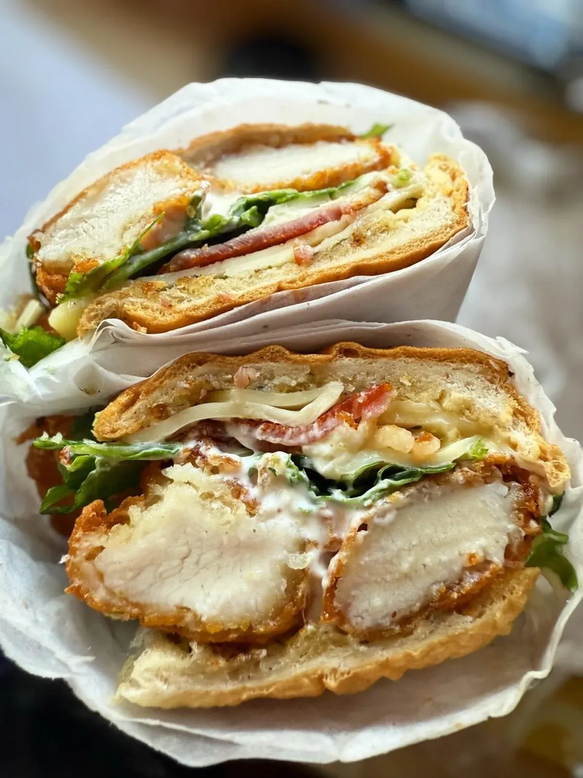 a freshly-cut loaded chicken and bacon bagel from crumbs & grind , crispy chicken, melted cheese, and fresh salad , wrapped and ready to share on social